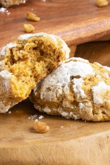 Close up of two pumpkin with applesauce and walnut cookies on a wooden board with a bite out of one.