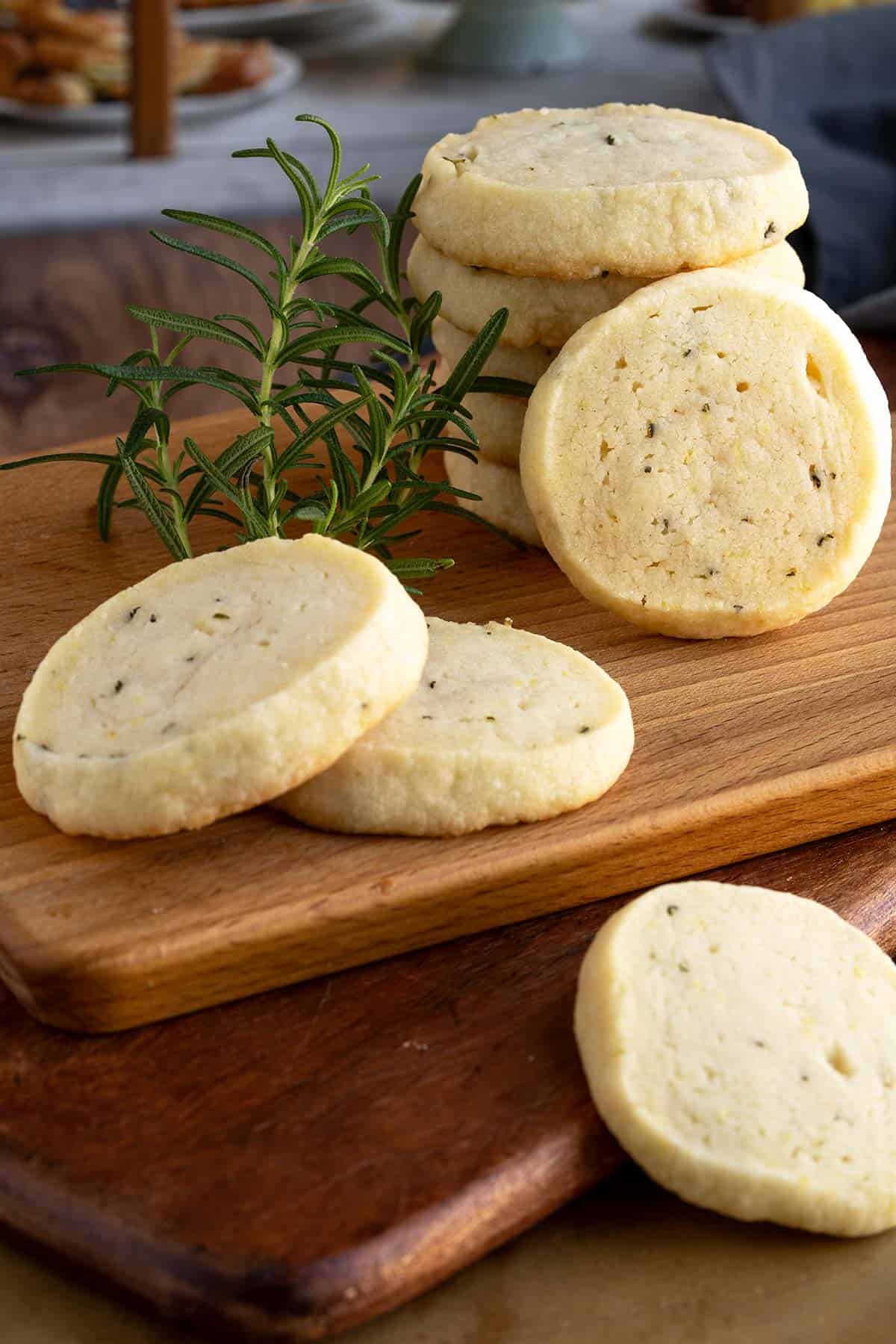 Rosemary with lemon and honey shortbread cookies stacked on a wooden board with a sprig of fresh rosemary.