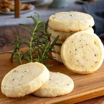 Rosemary lemon honey shortbread cookies stacked on a wooden board, with one cookie shown in front.