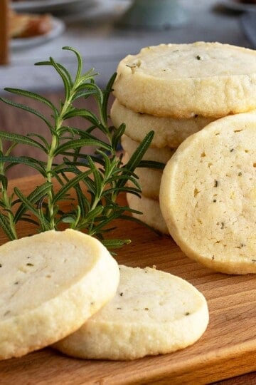 Rosemary lemon honey shortbread cookies stacked on a wooden board, with one cookie shown in front.