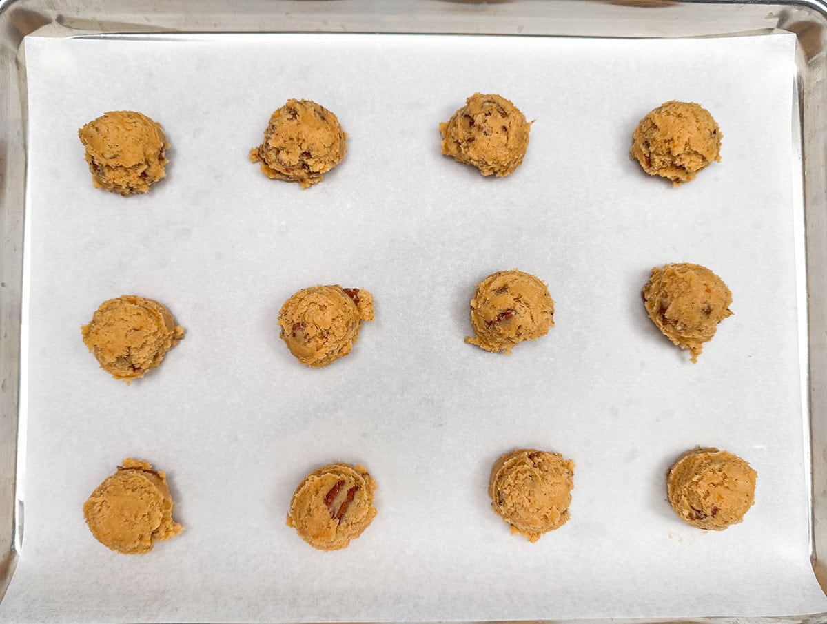 Scooped sweet potato pie cookie dough on a parchment paper lined cookie sheet pan.