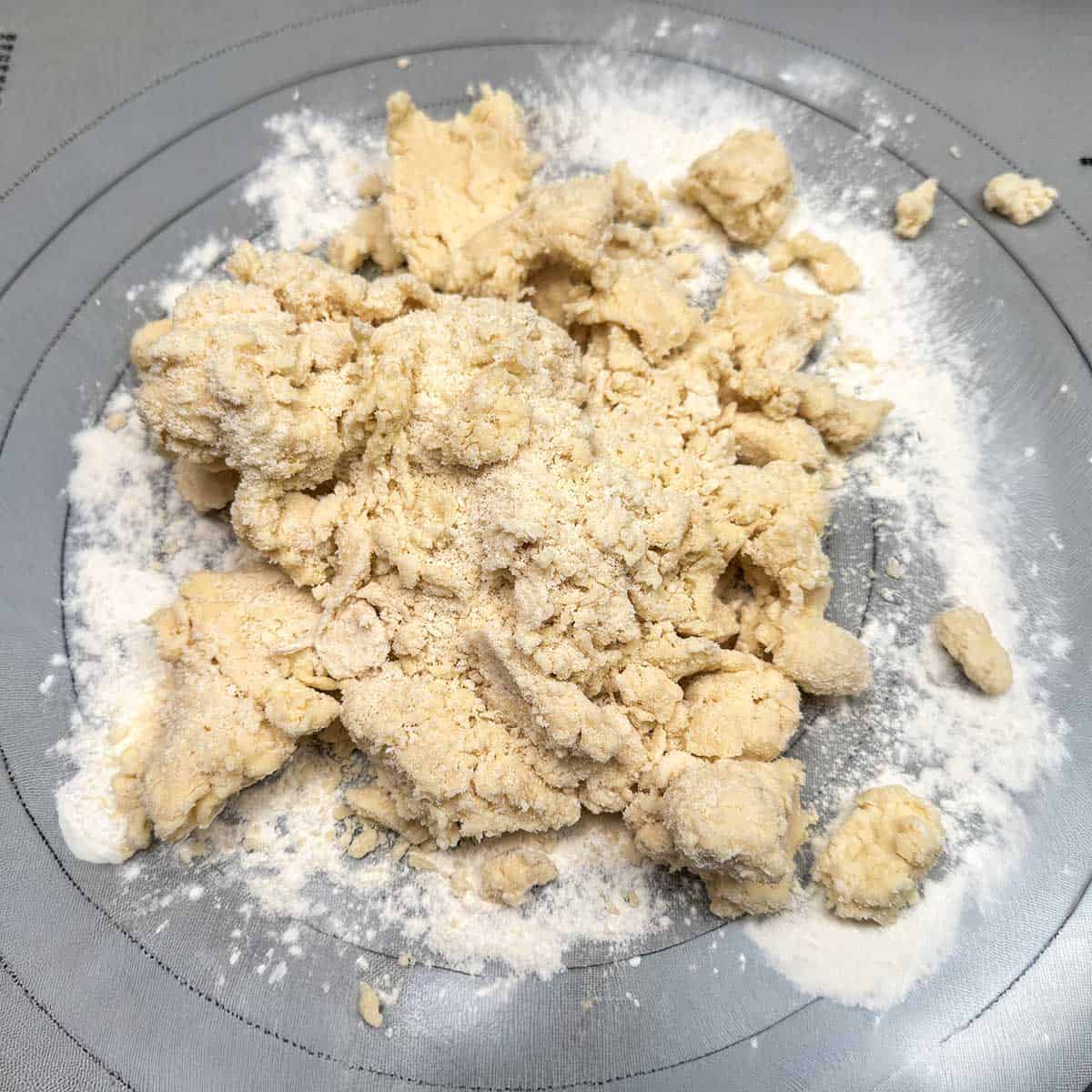 Mostly mixed cookie dough dumped onto lightly floured mat to be kneaded and ingredients brought together.