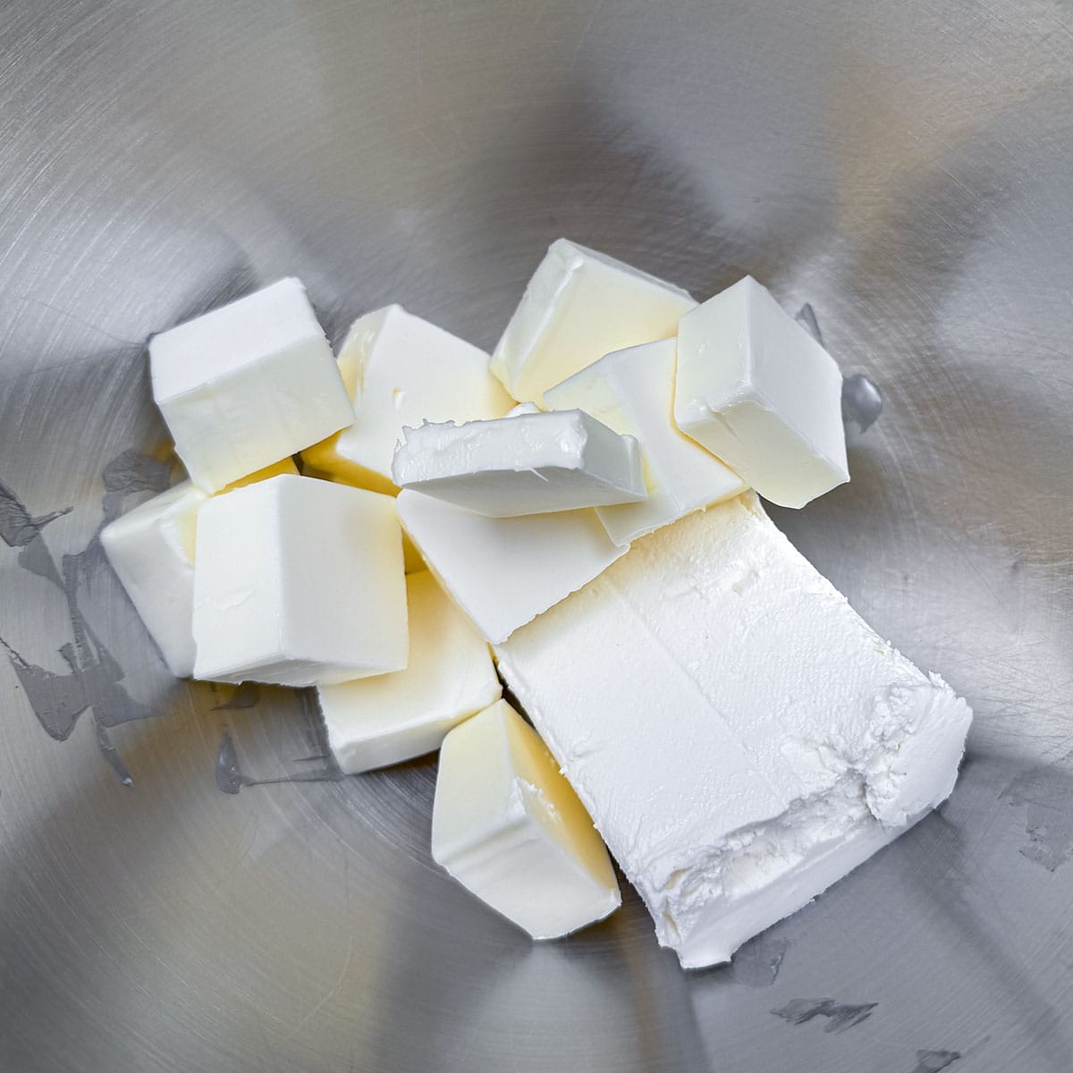 Block of cream cheese and cubed butter in a mixer bowl.