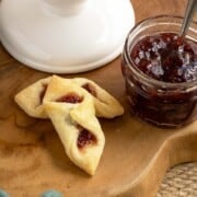 Red raspberry kolache cookies with a jar of the raspberry preserves on a wooden board.