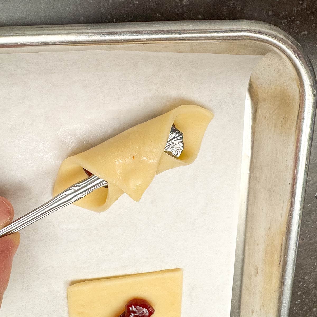 Sticking the handle of a long spoon between the fold over cookie dough and the raspberry preserves. This way you can press down and seal the corners.