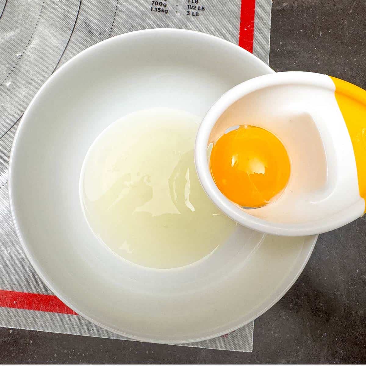 An egg separator that is on the side of a bowl. The egg white is to seal the opposite two corners over the raspberry preserves.