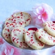 Sprinkle shortbread cookies on a plate with soft looking flowers around the plate.