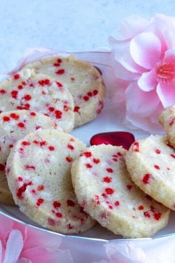 Sprinkle shortbread cookies on a plate with soft looking flowers around the plate.