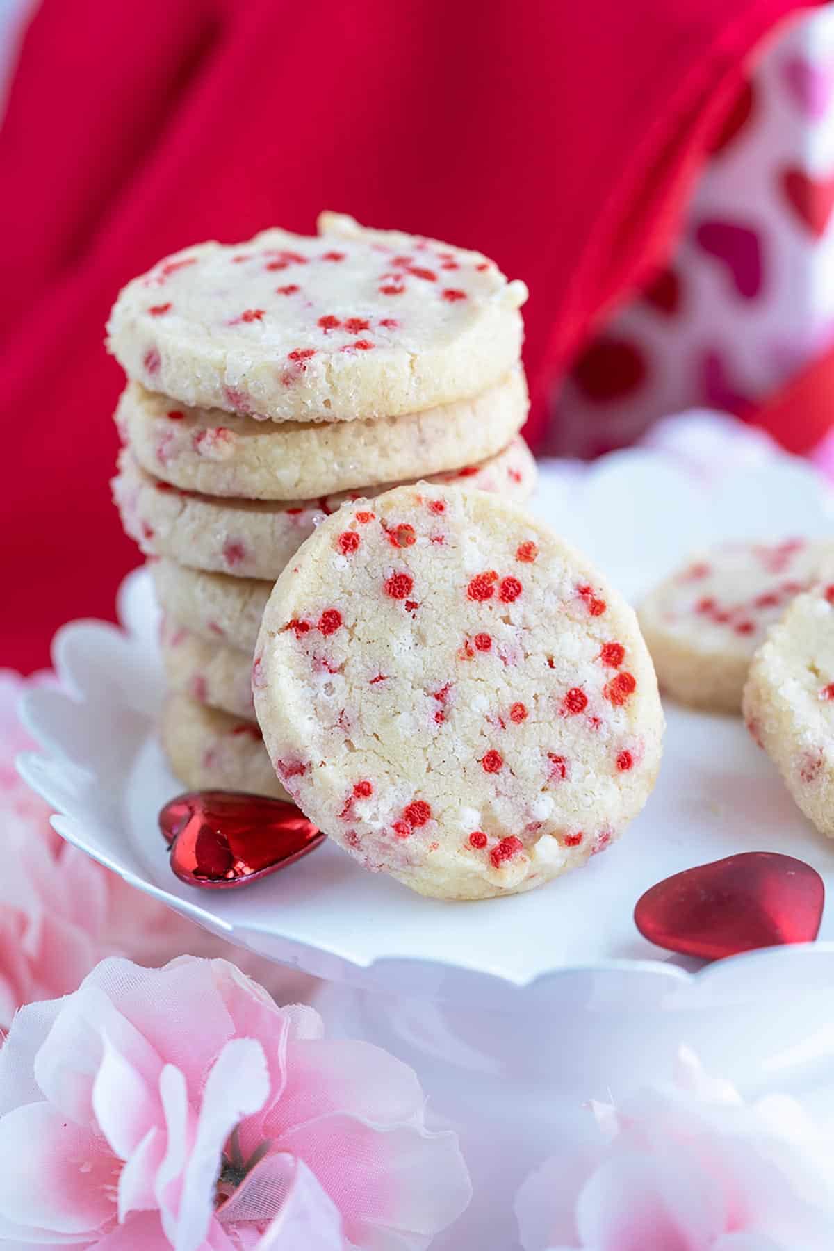 Sprinkle shortbread cookies stacked on a plate with one cookie on its end leaning against the stack.