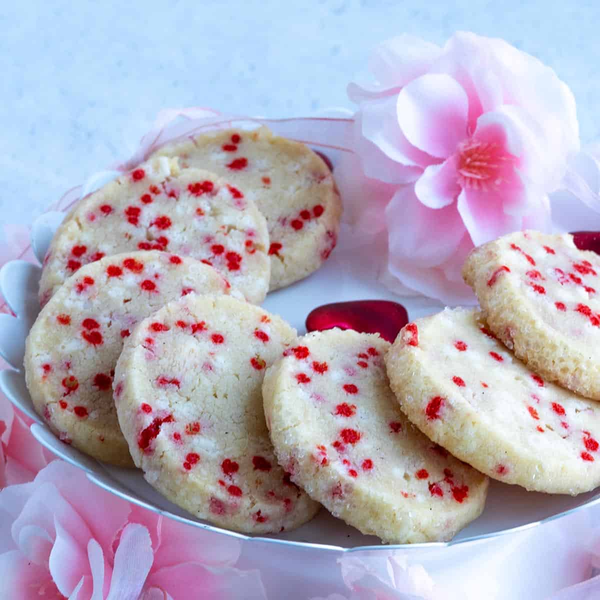 Sprinkle shortbread cookies on a plate with soft looking flowers around the plate.