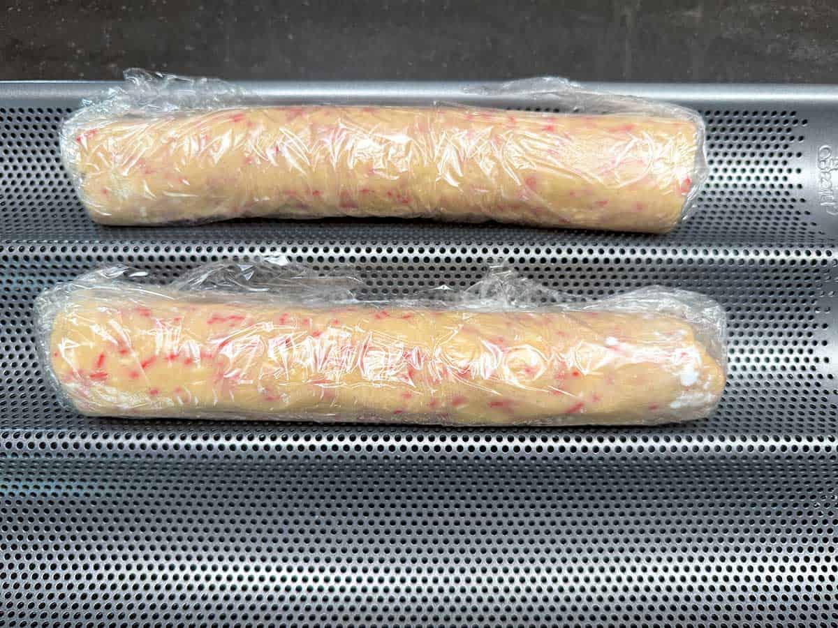 Two 9 inch cookie wrapped logs sitting on a baguette pan ready for the chill.