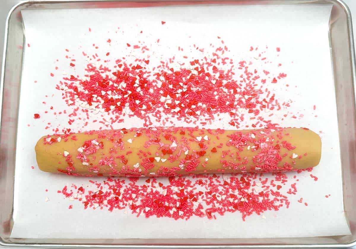Valentine colored jimmies that the combined two cookie doughs are being rolled in to stick to the outside.