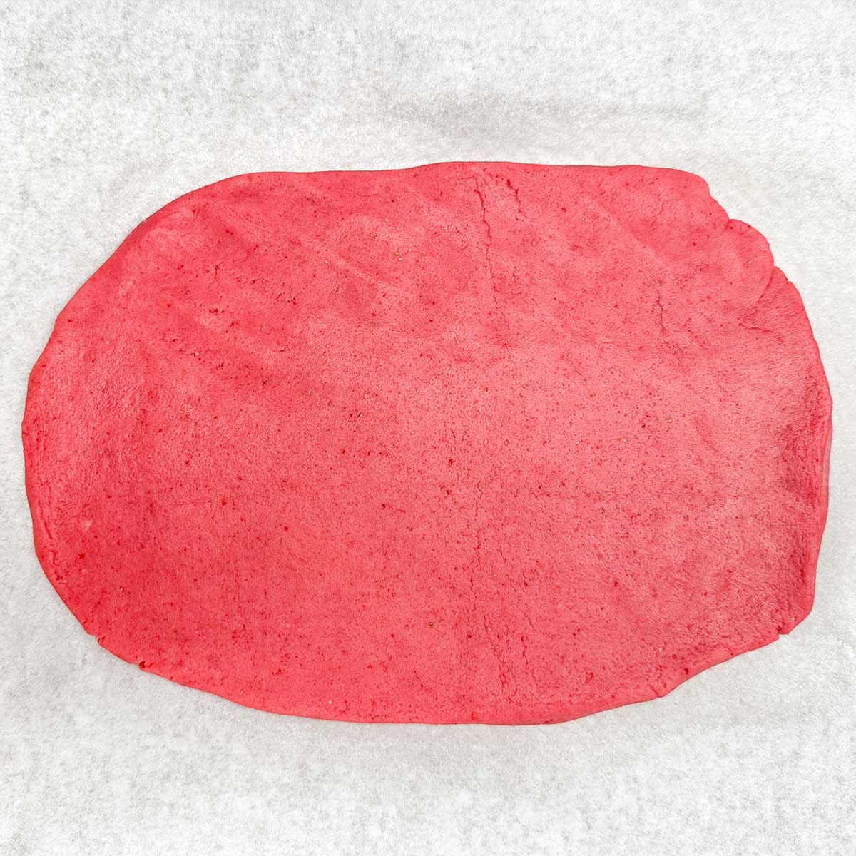 Strawberry flavored cookie dough rolled out onto a piece of parchment paper.