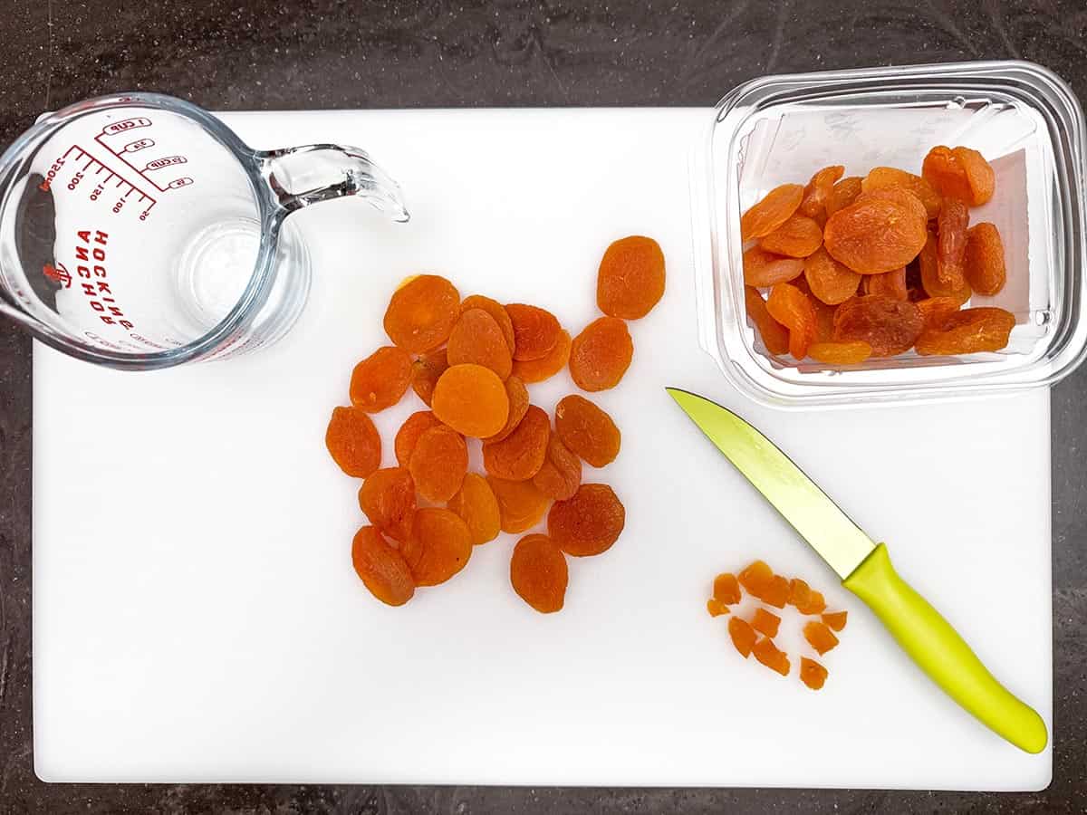 Cutting dried apricots with a sharp knife on a cutting board.