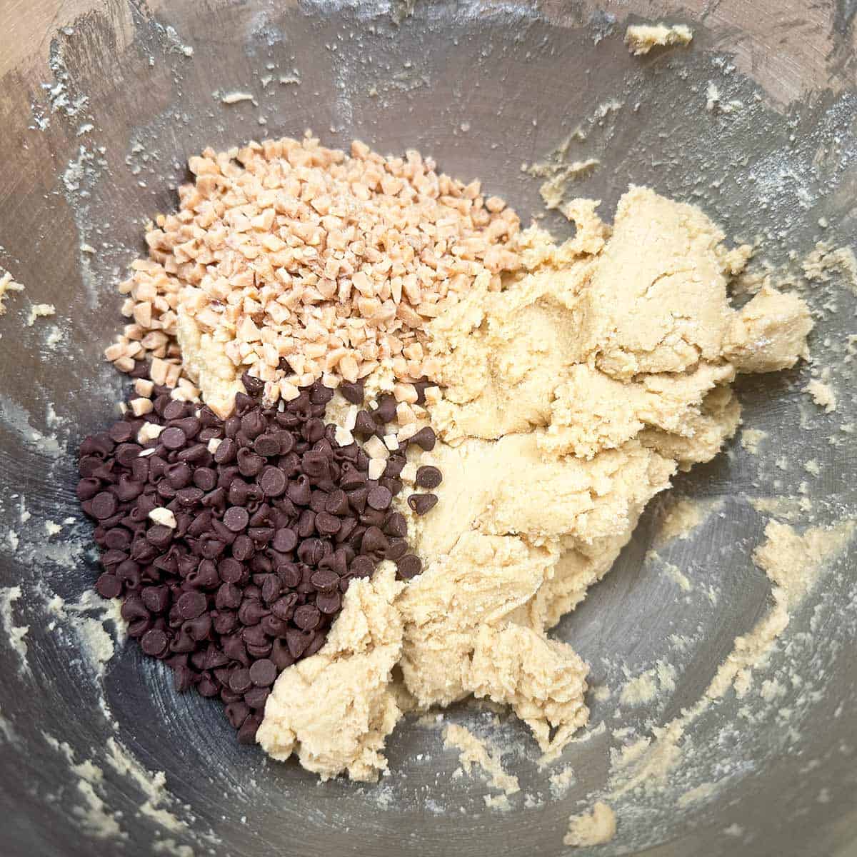 Adding mini chocolate chips and toffee bits to the cookie dough in the mixer bowl.