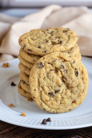Chocolate chip toffee cookies stacked on a plate with one cookie standing up so you see the front view.