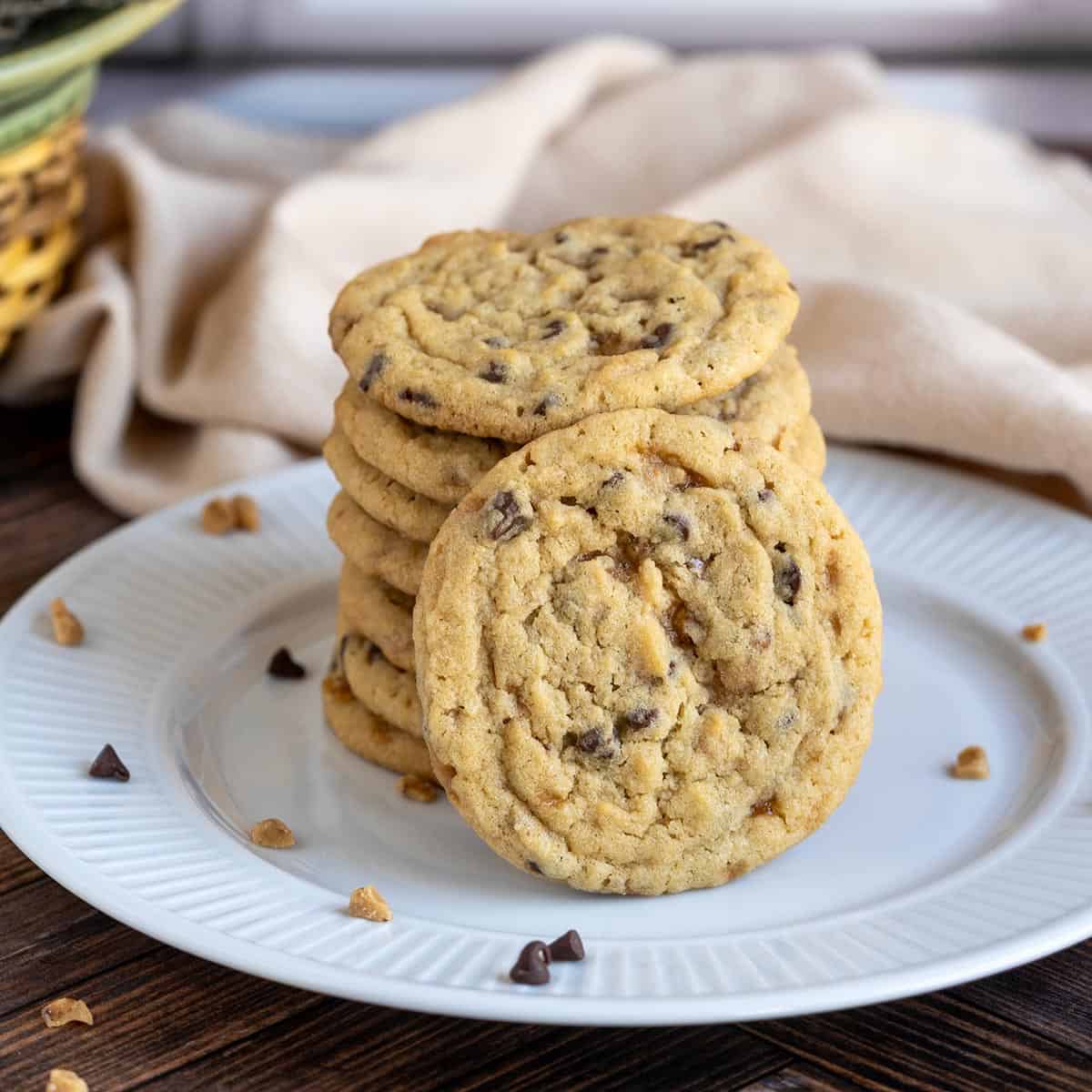 Chocolate chip toffee cookies stacked on a plate with one cookie standing up so you see the front view.