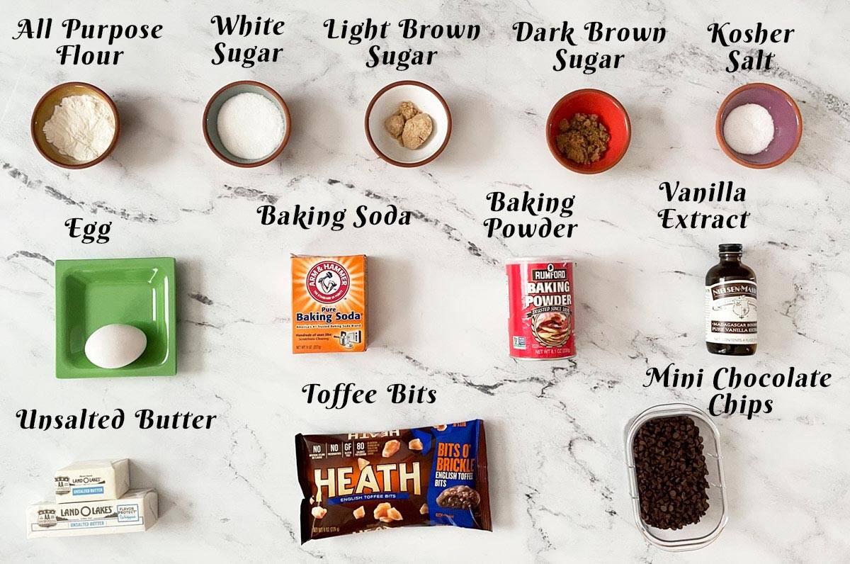Ingredients to make chocolate chip toffee cookies on a white board.