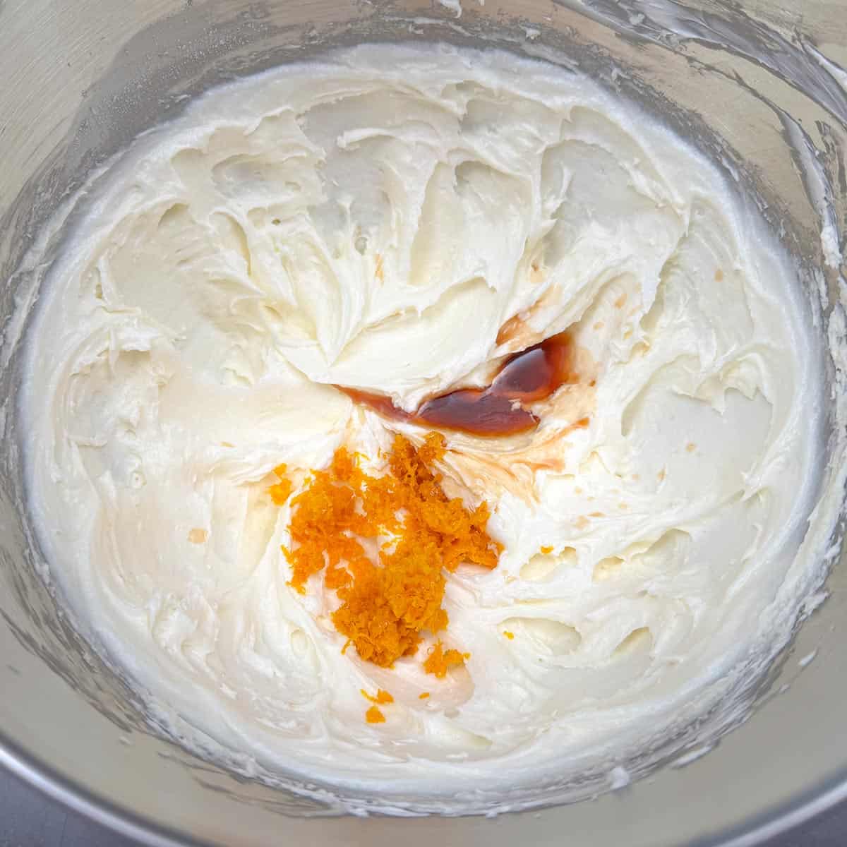 Adding the orange zest and vanilla extract to the sugar, butter, and cream cheese mixture.