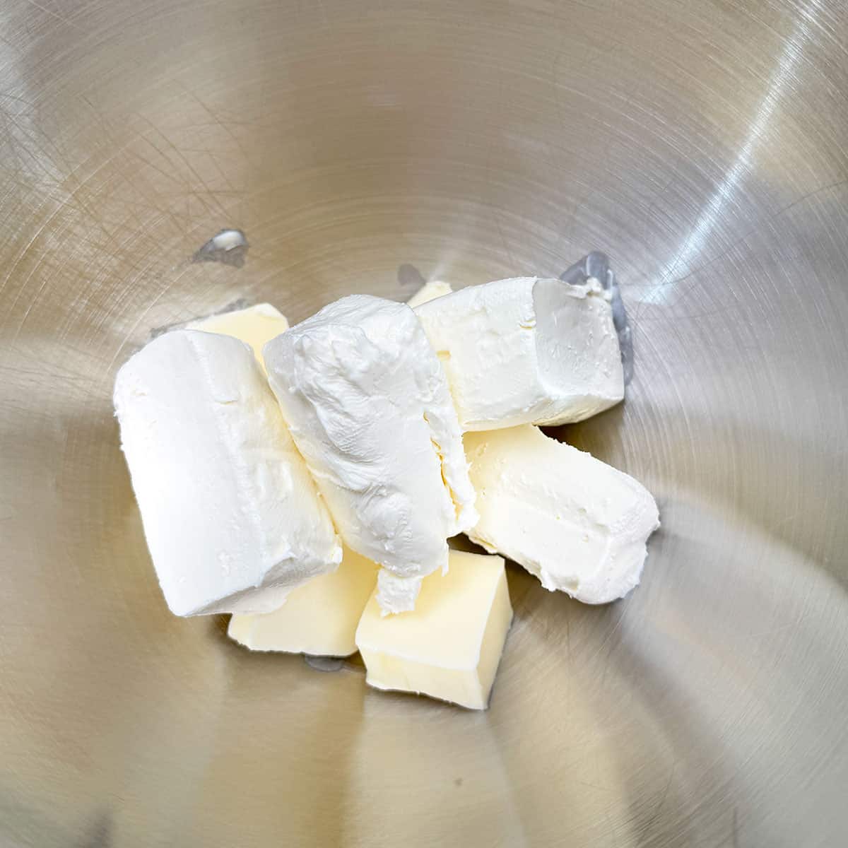 Cubed butter and cream cheese chunks in a mixer bowl.