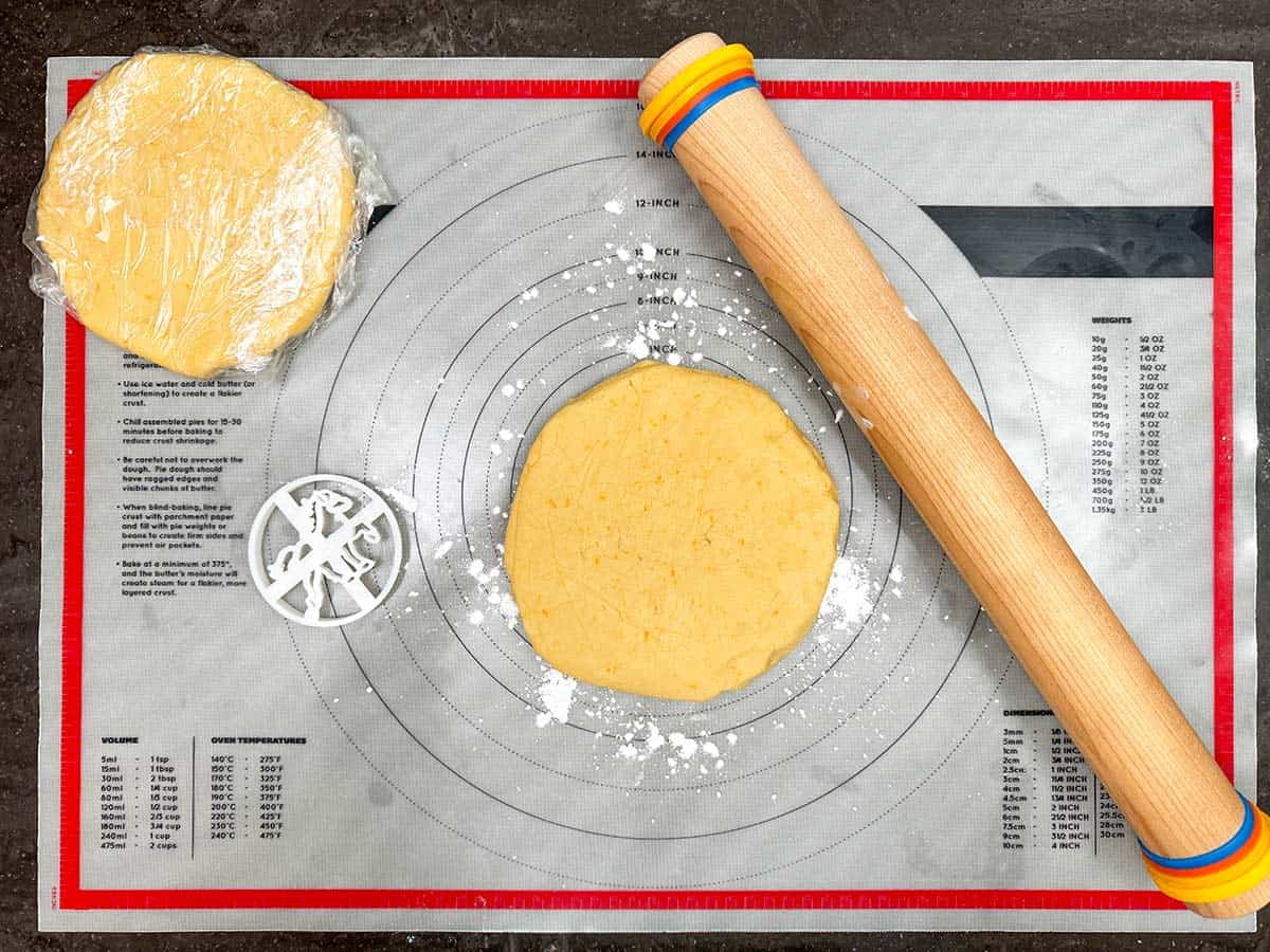 Rolling pin, cookie cutter, disks of cookie dough on a pastry mat.