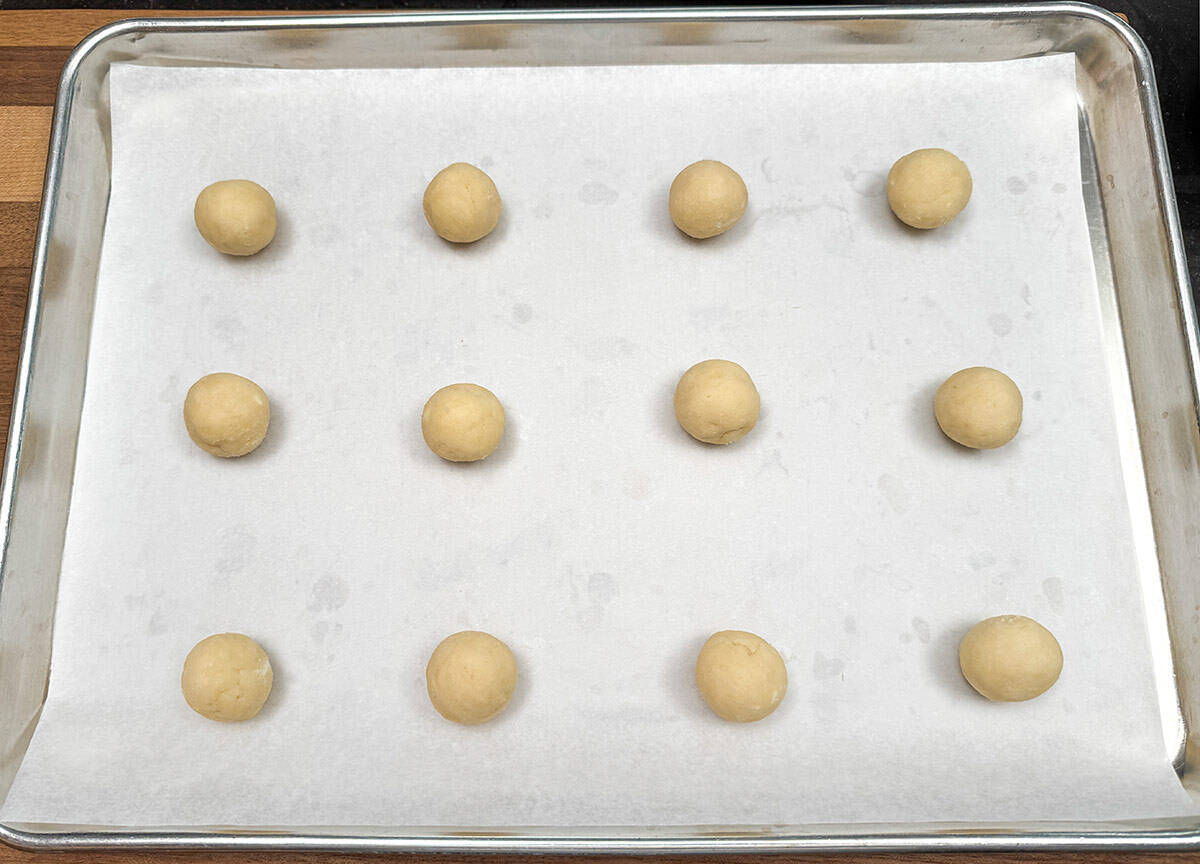 Twelve cookie dough balls on a parchment-lined cookie sheet pan.