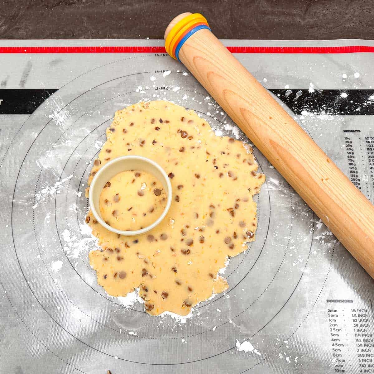 Rolled out cookie dough and round cookie cutter on a pastry sheet with rolling pin.