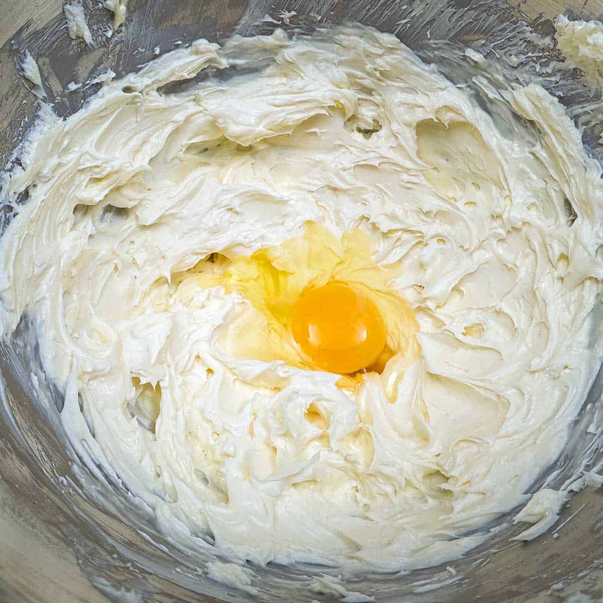 Adding the one of the eggs to the cream cheese mixture.
