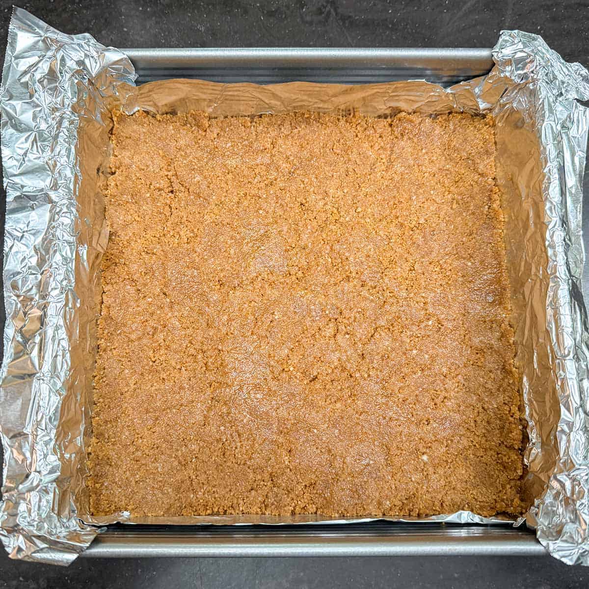 Crust mixture that has been pressed into the bottom of the tin-foiled lined pan for the crust.