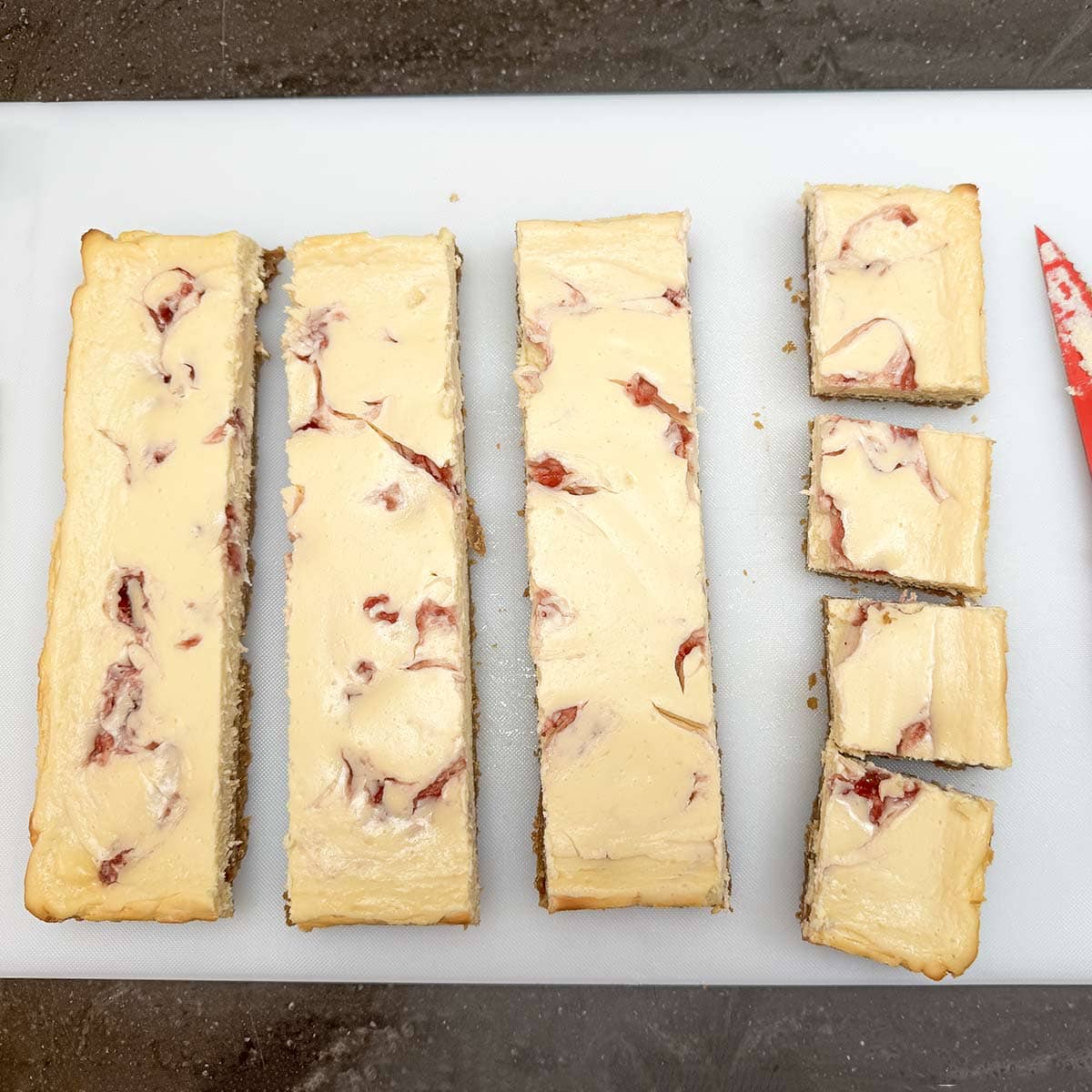 Baked strawberry key lime cheesecake strips getting cut into four pieces per strip.