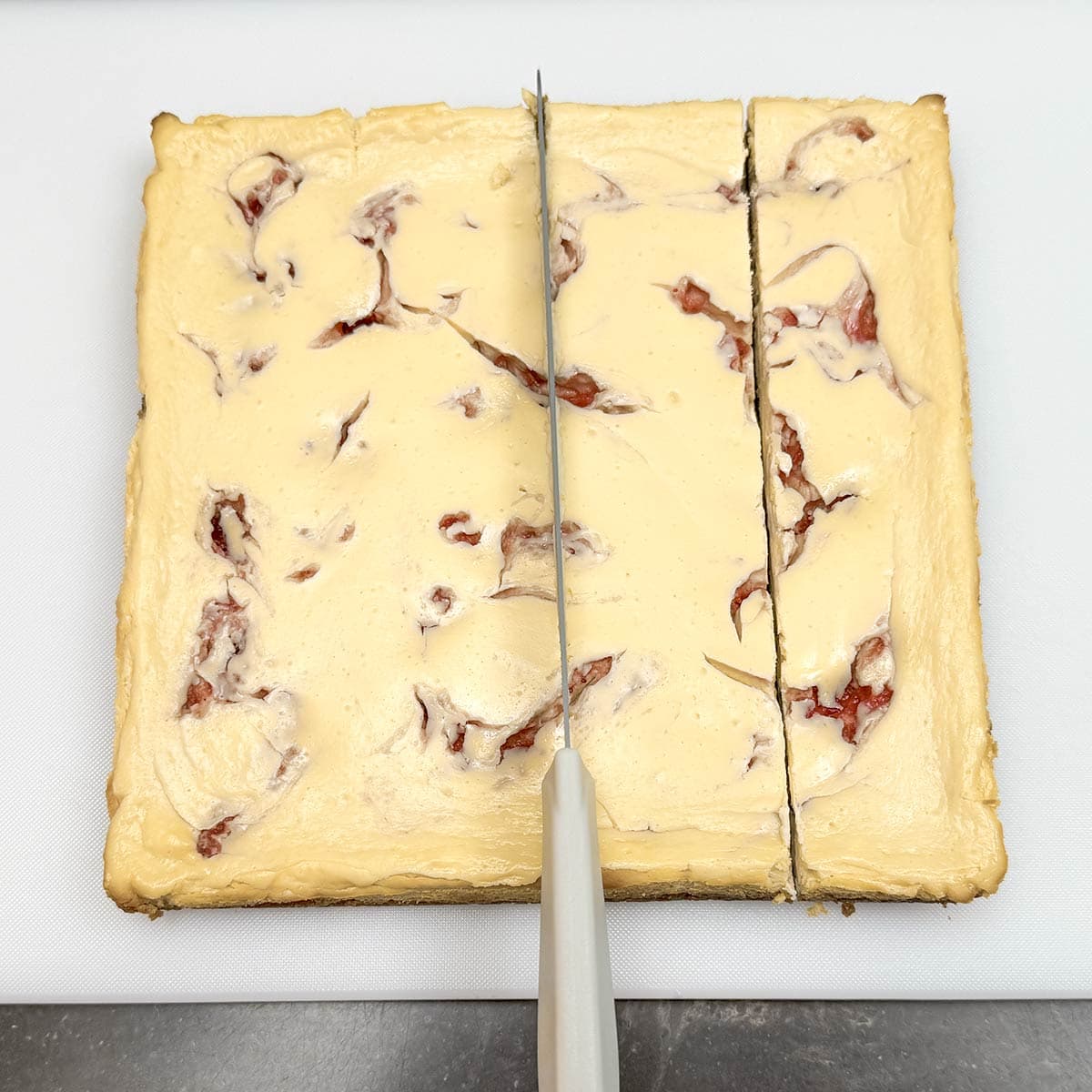 Baked strawberry key lime cheesecake getting cut into strips.