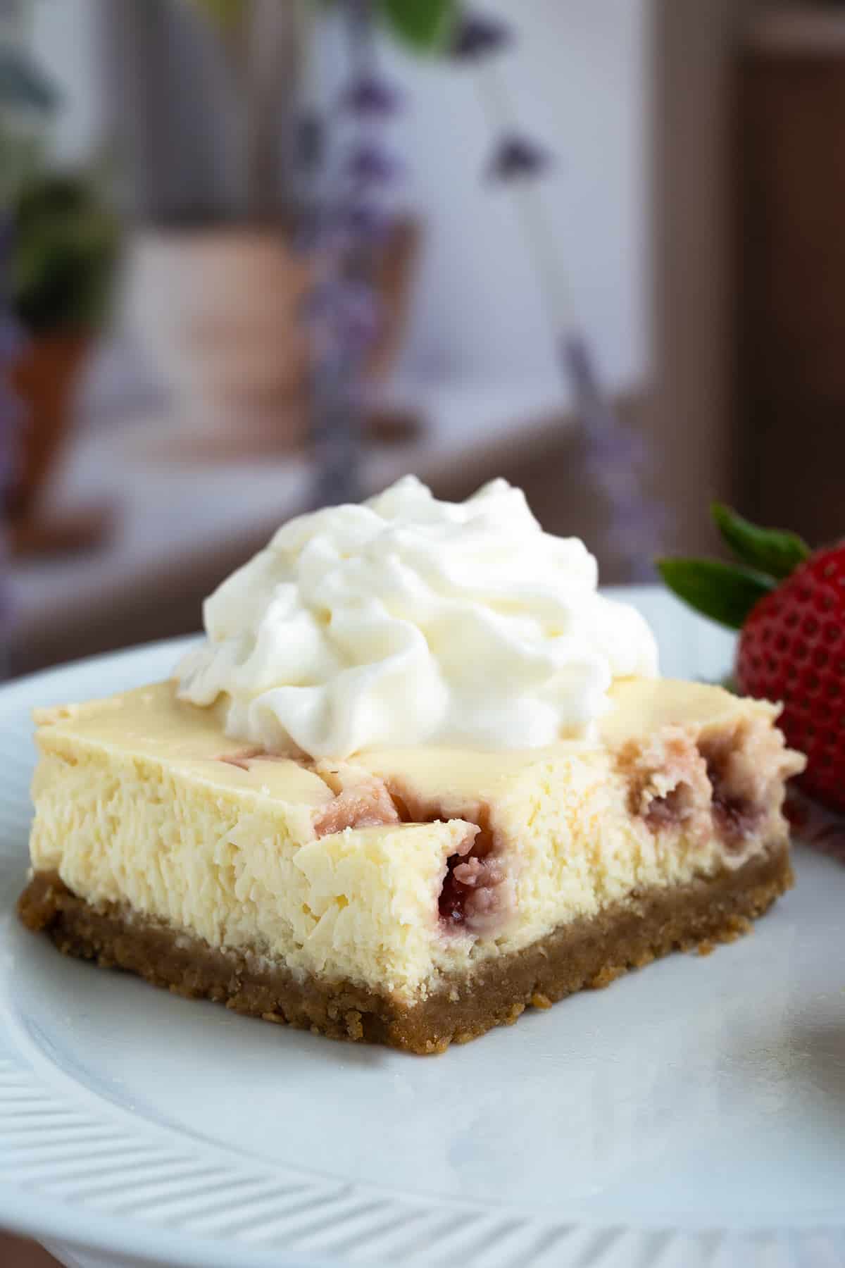 Strawberry key lime cheesecake with whip cream on top on a serving plate.