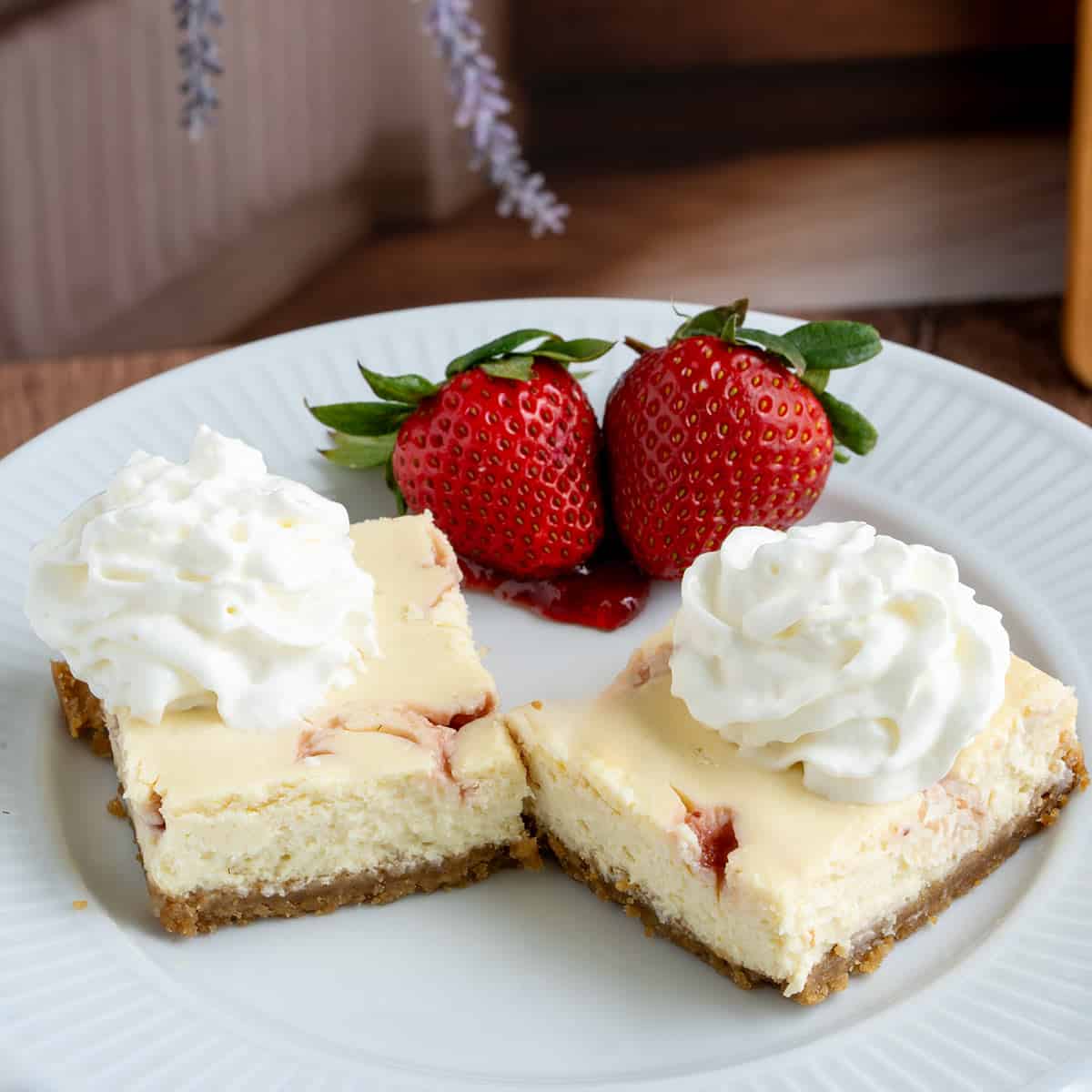 Two strawberry key lime cheesecake squares with whip cream and two strawberries behind the cheesecake pieces.