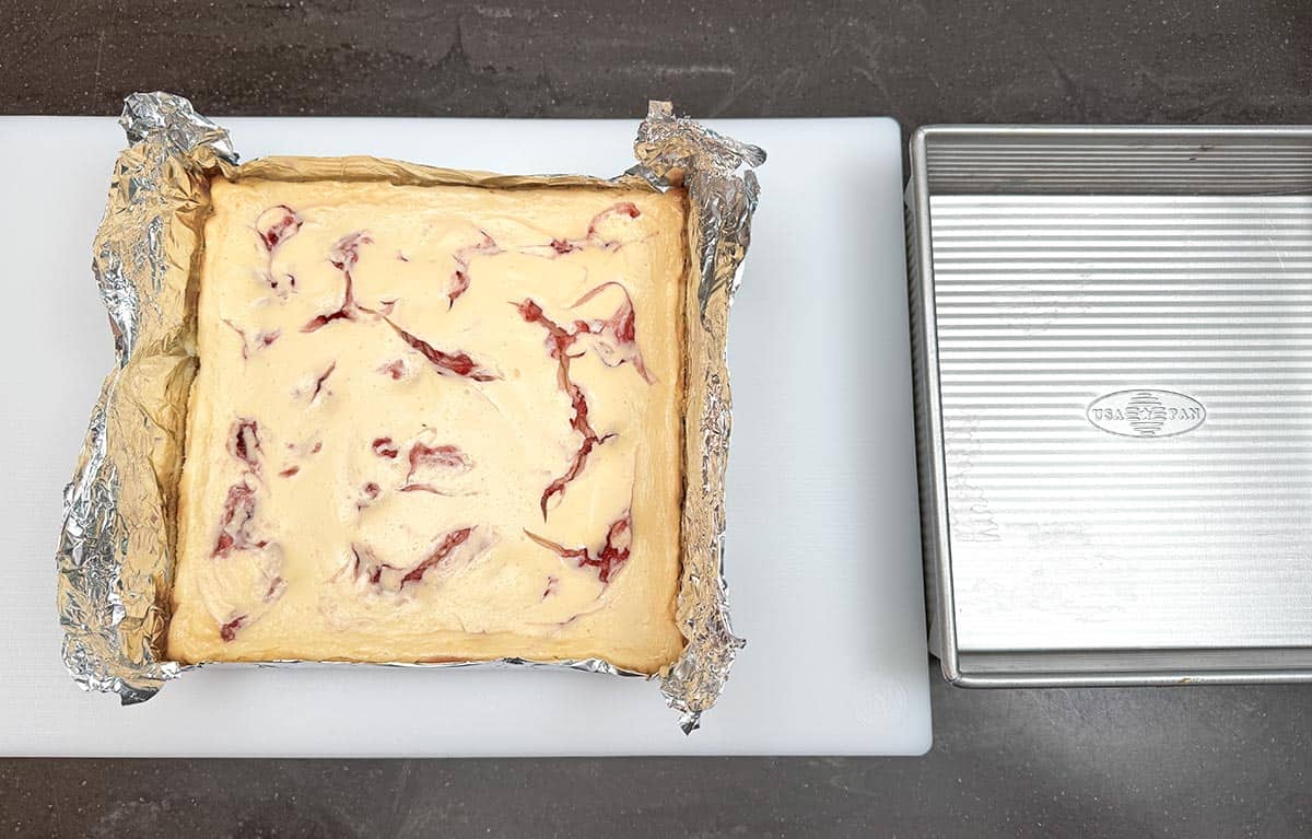 Lifting the whole cheesecake out of the pan but the tin foil handles on the side.
