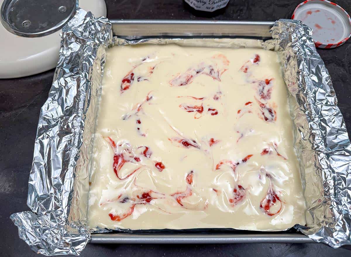 Cheesecake in pan with the strawberry preserves that have been swirled through the wet ingredients.