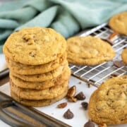 Chocolate chip cookies with glazed pecans stacked on a tray with nuts and chocolate chips laying around.