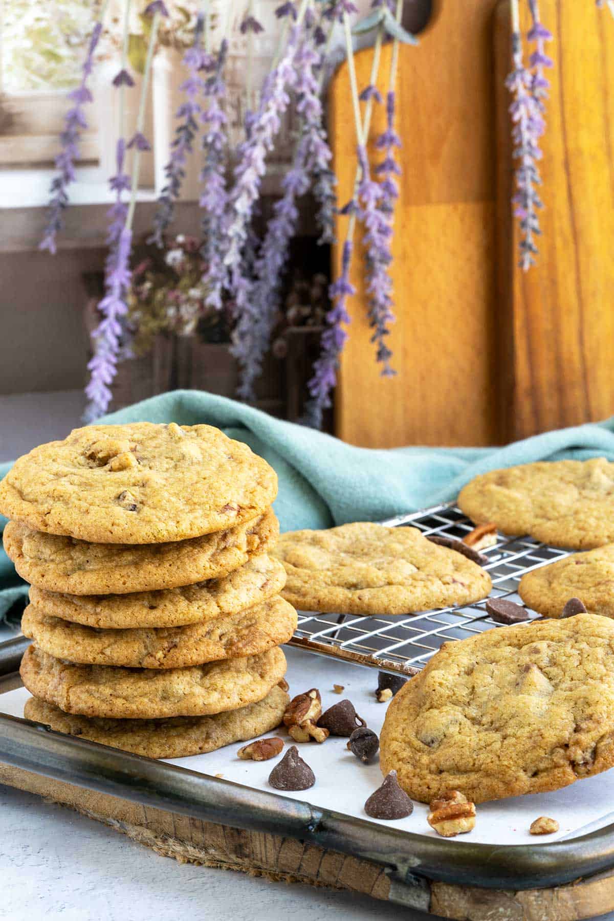 Chocolate chip cookies with glazed pecans stacked on a tray in front of a window.