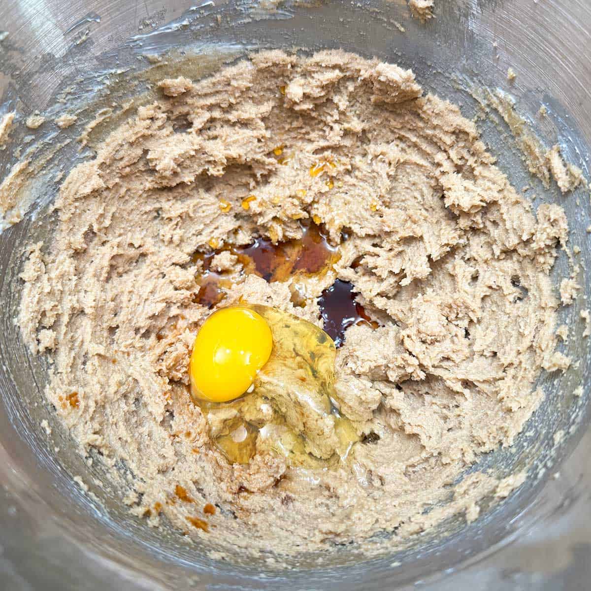 Adding egg, maple syrup, and vanilla extract to the butter-sugar mixture in a mixer bowl.