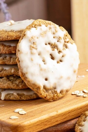 Maple cinnamon iced oatmeal cookies stacked with on front view leaning against the stack of cookies.