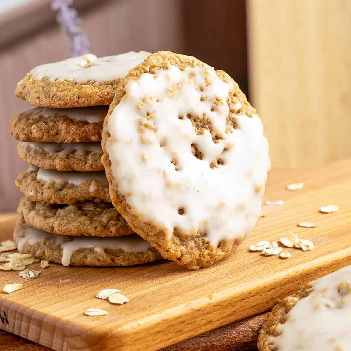 Maple cinnamon iced oatmeal cookies stacked with on front view leaning against the stack of cookies.