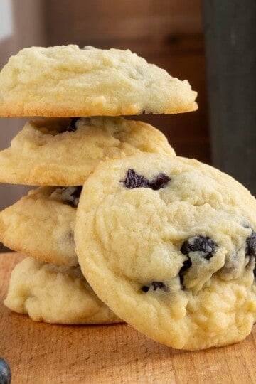 Fresh blueberry lemon maple cookies in a stack with one showing the front side with plump blueberries showing through.