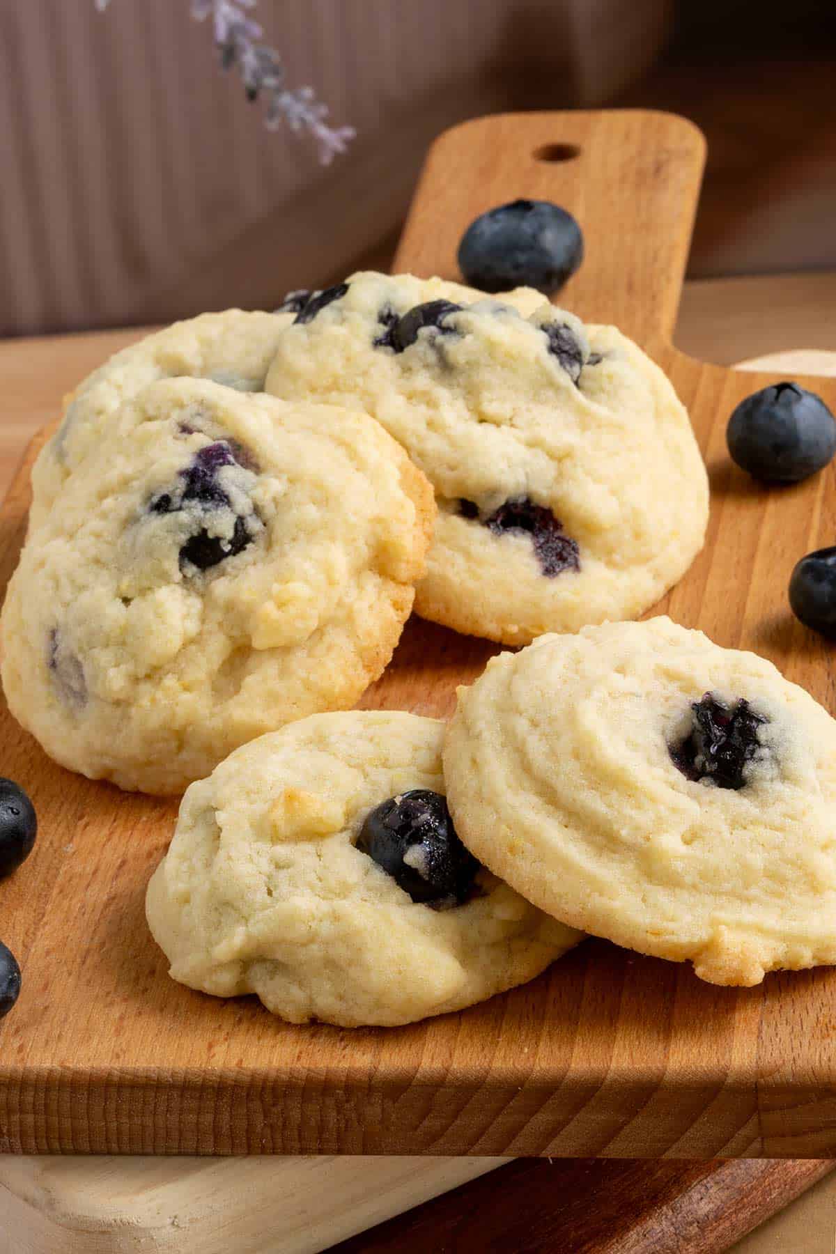 Fresh blueberry lemon maple cookies laying on a wooden board with whole blueberries laying around the cookies.