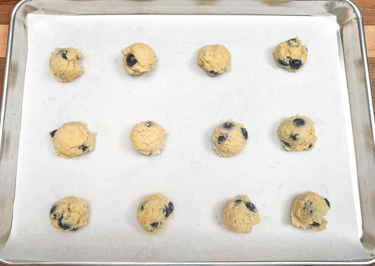 Twelve scooped blueberry lemon maple cookies on a parchment-lined sheet pan.