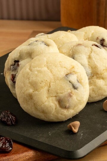 Cherry caramel sea salt cookies on a board with cherries and caramel sea salt chips laying around.