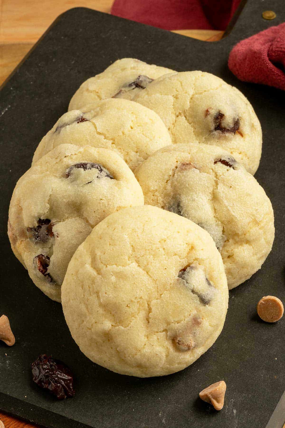 Cherry caramel sea salt cookies on a board with cherries and caramel sea salt chips laying around.