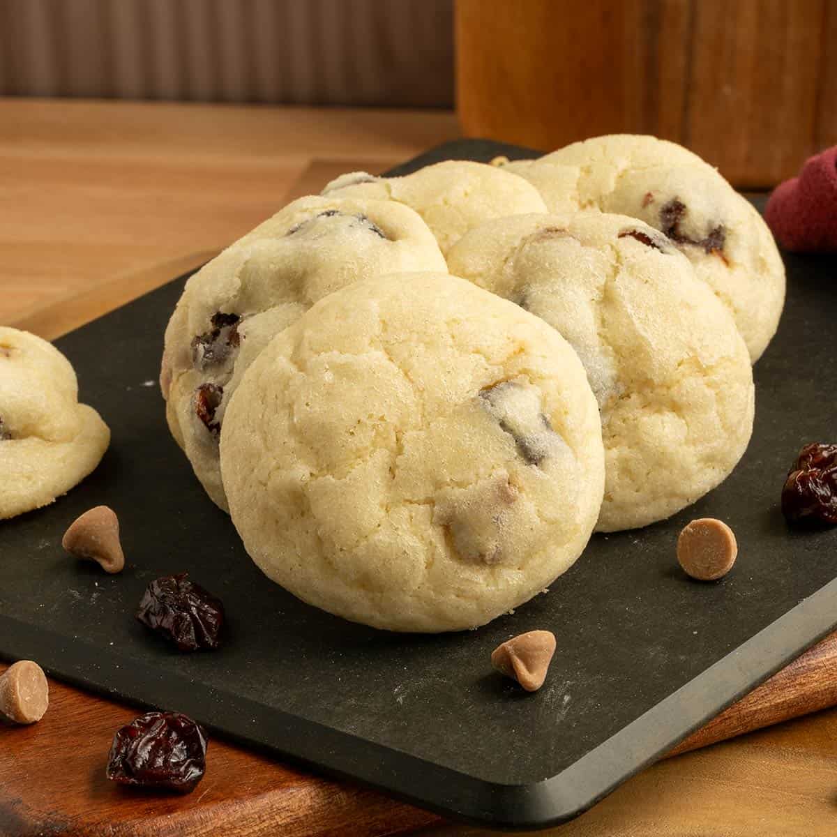 Cherry caramel sea salt cookies on a board with cherries and caramel sea salt chips laying around.