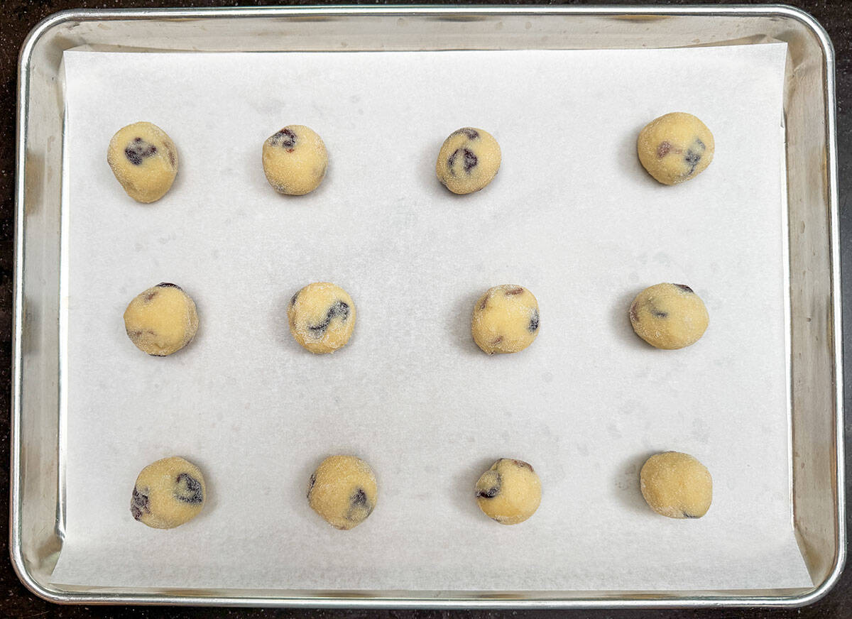 Twelve balls of cookie dough rolled in fine sugar and placed on a parchment-lined sheet pan.