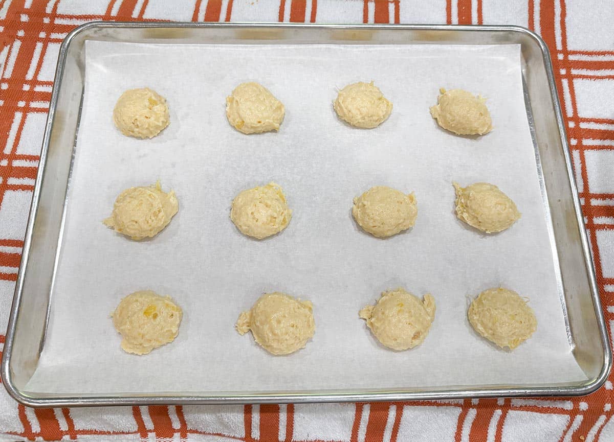 Pineapple coconut cookie dough scooped onto a parchment lined sheet pan.