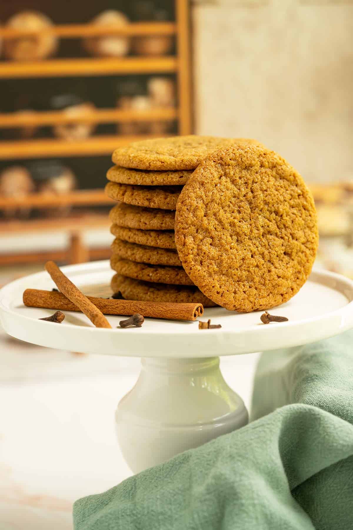 Chewy Ginger Molasses Cookies on a stand with cinnamon sticks and clove spread around the dish.