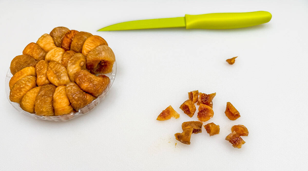 Container of figs with one fig's stem cut off and the fig cut into small pieces.